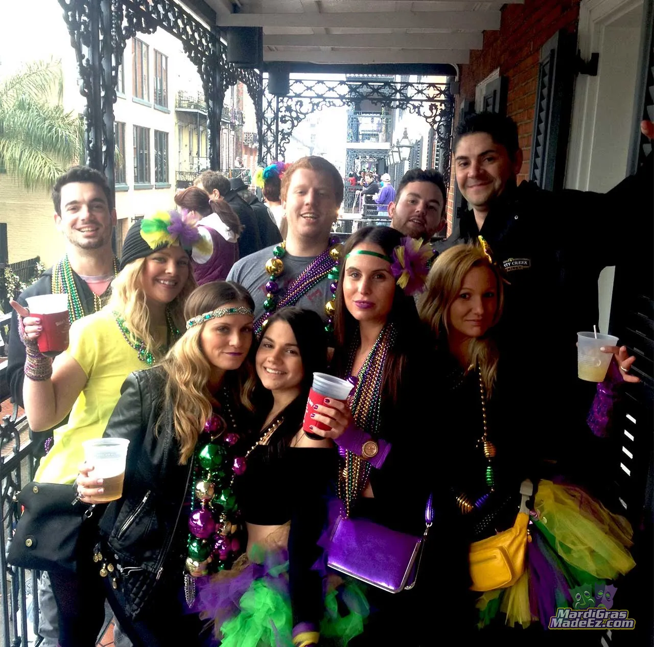 A group in Mardi Gras beads celebrating together on a Bourbon Street balcony