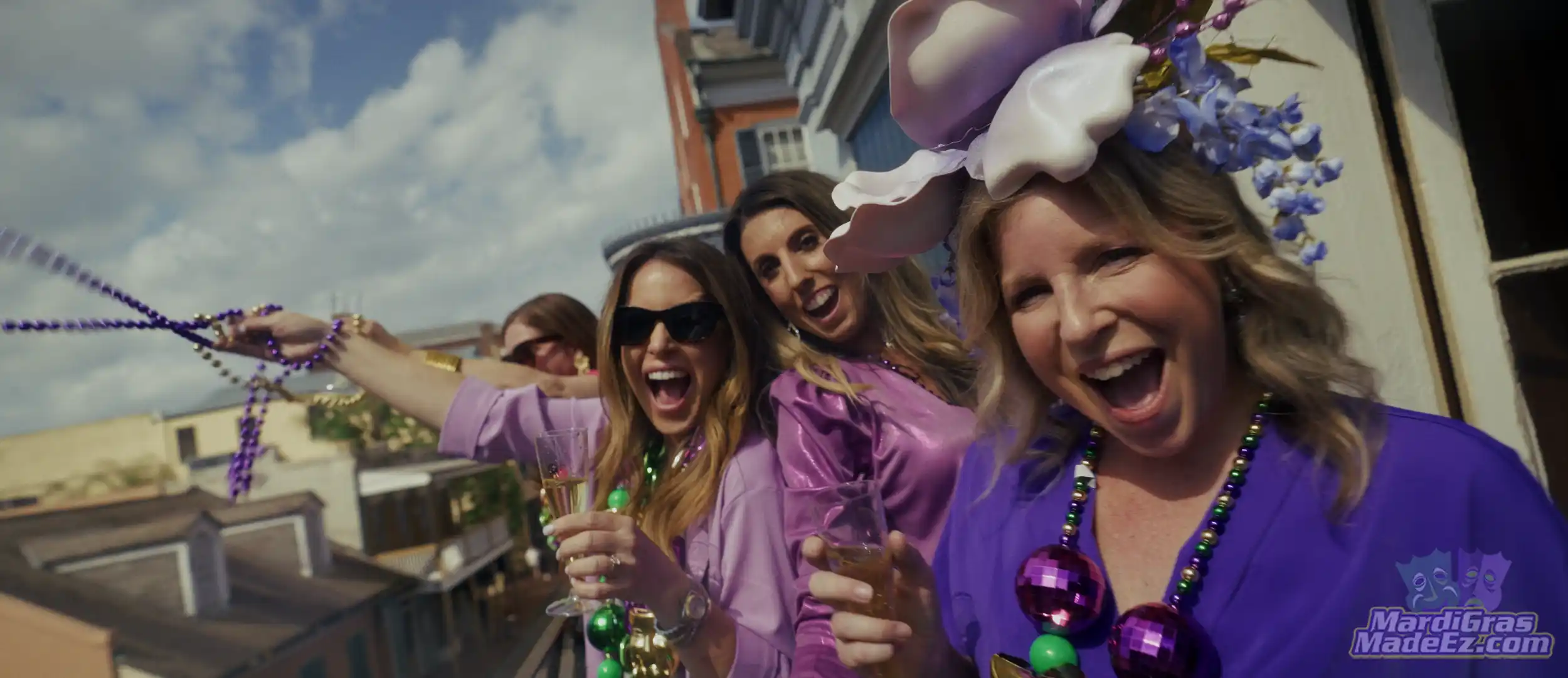 Guests in purple and green laughing and throwing beads from a balcony above the street